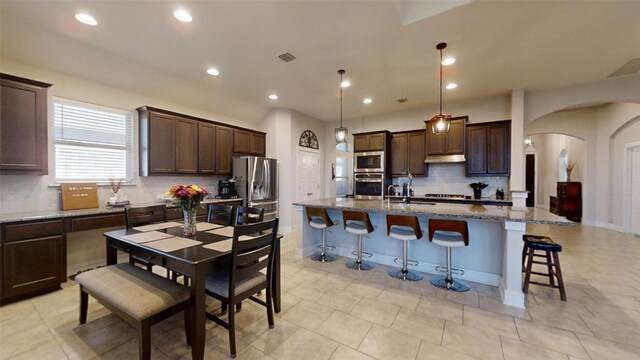 kitchen featuring stainless steel appliances, a breakfast bar, an island with sink, dark stone counters, and pendant lighting