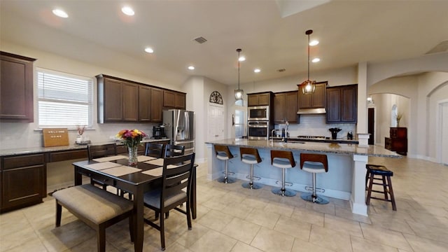 kitchen featuring stainless steel appliances, arched walkways, under cabinet range hood, and dark brown cabinets