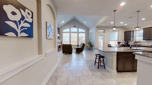 kitchen with vaulted ceiling, a breakfast bar, light stone counters, dark brown cabinets, and decorative light fixtures