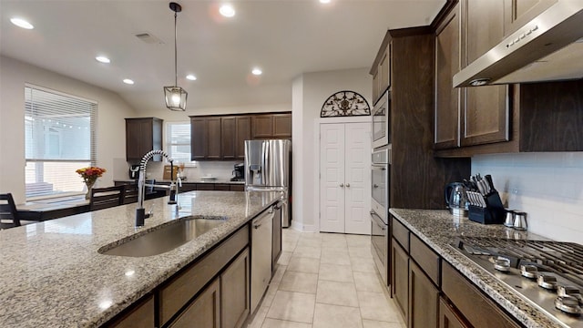 kitchen featuring stainless steel appliances, light stone countertops, pendant lighting, dark brown cabinetry, and sink