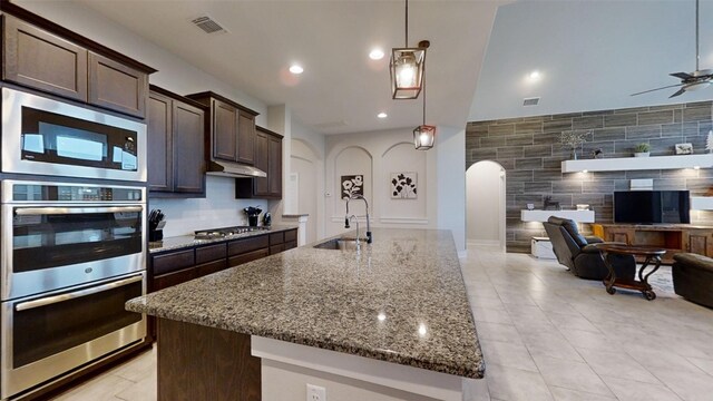 kitchen with stainless steel appliances, stone counters, pendant lighting, sink, and dark brown cabinets