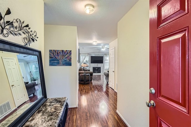 foyer featuring dark wood-style floors, a fireplace, visible vents, a textured ceiling, and baseboards