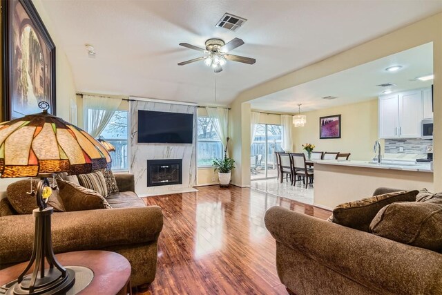 living room featuring ceiling fan with notable chandelier, wood-type flooring, a high end fireplace, and sink