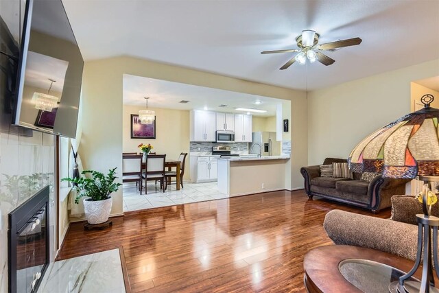 living room with ceiling fan with notable chandelier, sink, light wood-type flooring, and wine cooler