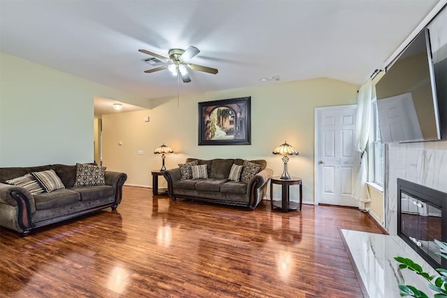 living room featuring dark wood-style floors, vaulted ceiling, a tiled fireplace, and a ceiling fan