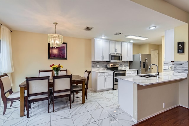 kitchen with kitchen peninsula, stainless steel appliances, tasteful backsplash, an inviting chandelier, and white cabinets