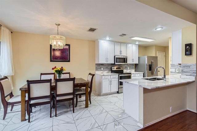 kitchen with a peninsula, a sink, visible vents, white cabinets, and appliances with stainless steel finishes