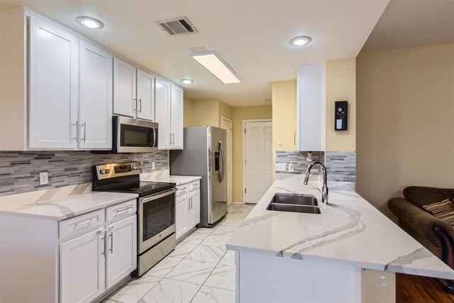 kitchen with appliances with stainless steel finishes, white cabinetry, light stone counters, and sink