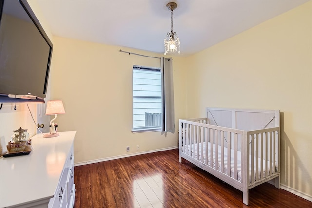 bedroom featuring dark wood-type flooring, a chandelier, and a nursery area