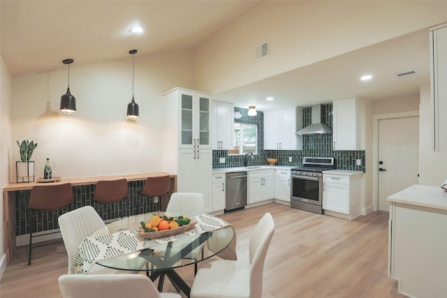 kitchen featuring pendant lighting, white cabinetry, sink, stainless steel appliances, and wall chimney range hood