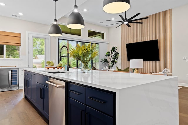 kitchen featuring hanging light fixtures, beverage cooler, a kitchen island with sink, blue cabinetry, and sink