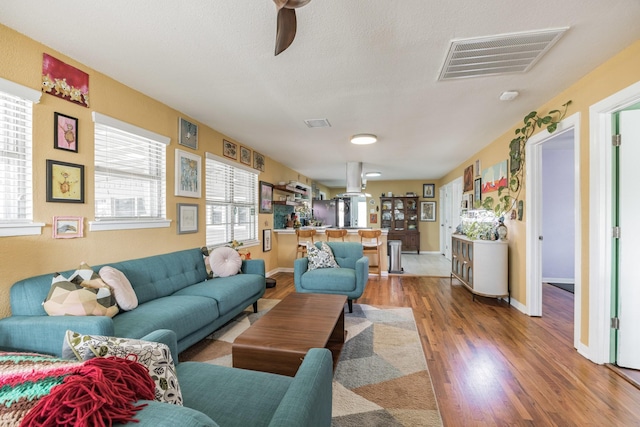 living room with a textured ceiling, wood-type flooring, and ceiling fan