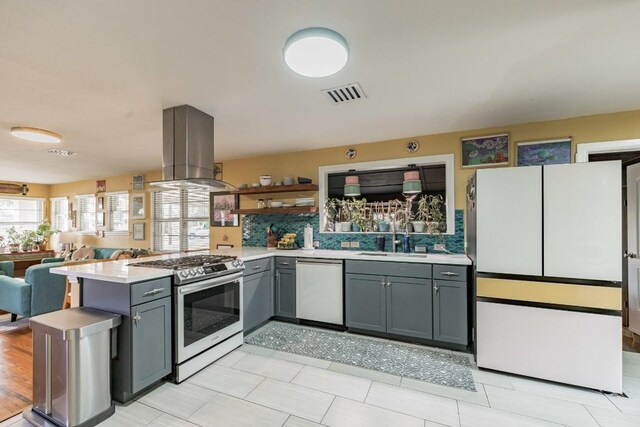 kitchen with island range hood, gray cabinetry, stainless steel appliances, kitchen peninsula, and sink