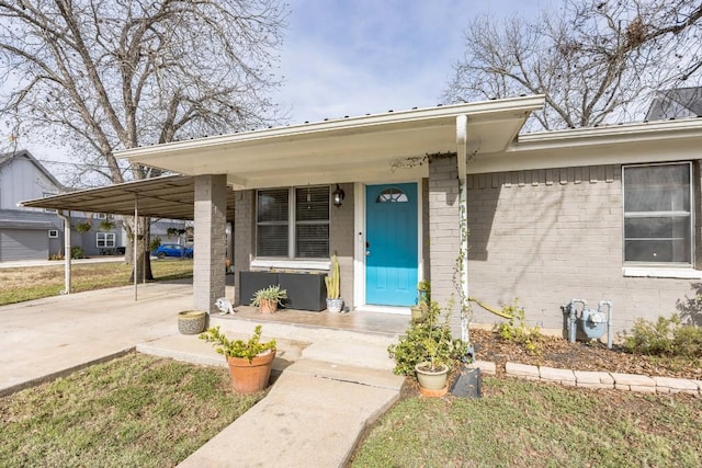 view of exterior entry with brick siding, a porch, concrete driveway, and a carport