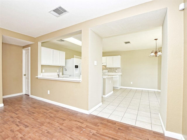 kitchen featuring white cabinets, a chandelier, kitchen peninsula, and white fridge with ice dispenser