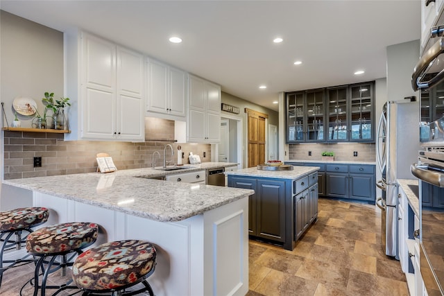 kitchen with white cabinetry, kitchen peninsula, light stone counters, and sink