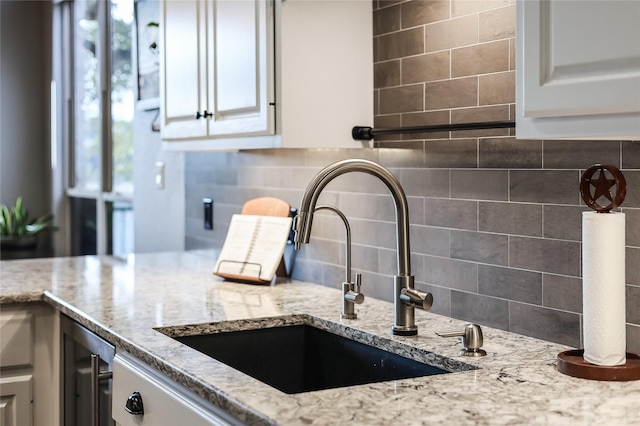 kitchen featuring light stone countertops, white cabinetry, decorative backsplash, and sink