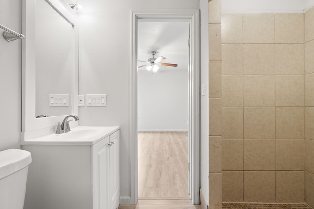 bathroom with wood-type flooring, toilet, vanity, ceiling fan, and a tile shower