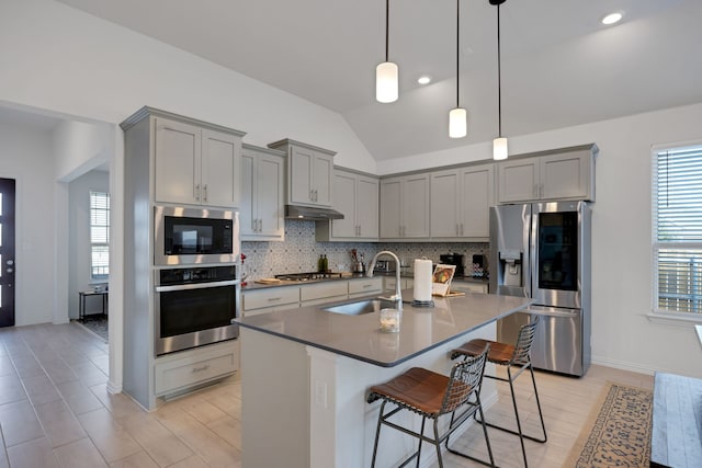 kitchen with sink, lofted ceiling, a breakfast bar area, a center island with sink, and appliances with stainless steel finishes