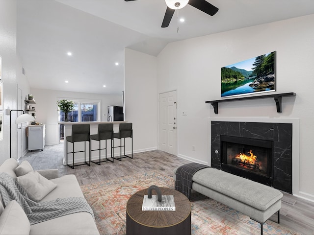 living room featuring a premium fireplace, ceiling fan, vaulted ceiling, and light hardwood / wood-style floors