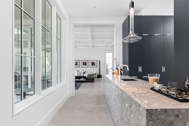 interior space featuring coffered ceiling, pendant lighting, light stone counters, beam ceiling, and sink