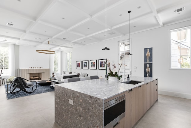 kitchen featuring light stone countertops, decorative light fixtures, a center island with sink, wall oven, and sink