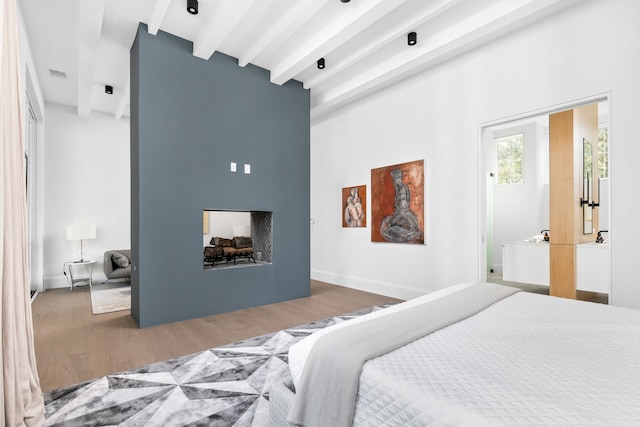 bedroom with a multi sided fireplace, hardwood / wood-style floors, and beamed ceiling