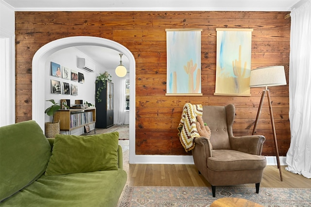 living area featuring a wall mounted air conditioner, wood-type flooring, crown molding, and wooden walls