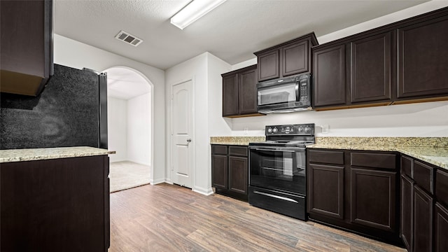 kitchen with a textured ceiling, dark brown cabinetry, black appliances, and hardwood / wood-style floors