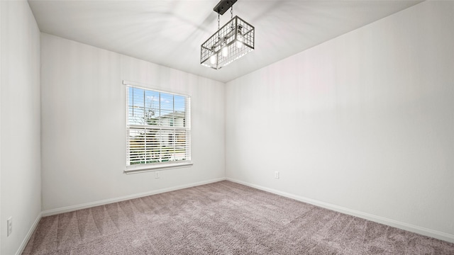 carpeted spare room featuring an inviting chandelier