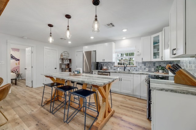 407 S Pine St, Georgetown, TX 78626 - kitchen featuring appliances with stainless steel finishes, light wood-style floors, decorative backsplash, a kitchen bar, and light stone countertops