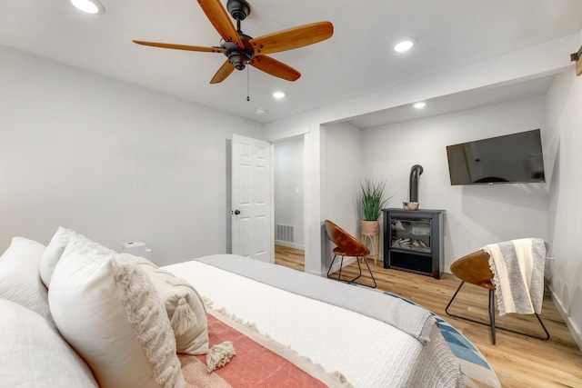 bedroom featuring light wood-type flooring, ceiling fan, and a wood stove