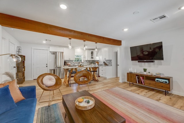 living room with beam ceiling, sink, and light wood-type flooring