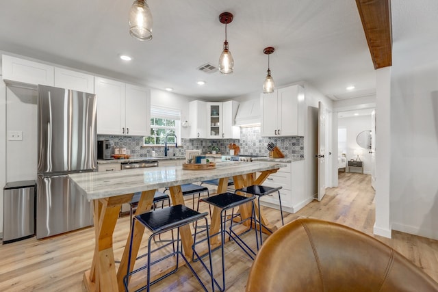 kitchen featuring stainless steel appliances, decorative light fixtures, white cabinets, light wood-type flooring, and light stone countertops