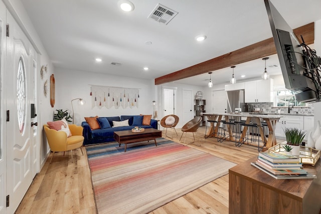 living room with beamed ceiling, sink, and light hardwood / wood-style floors