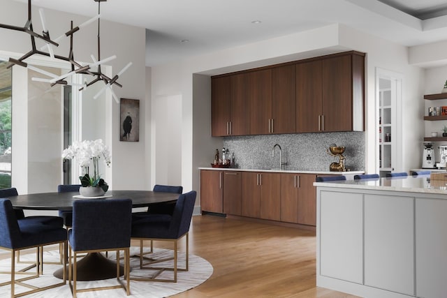 kitchen with a chandelier, hanging light fixtures, tasteful backsplash, light wood-type flooring, and sink