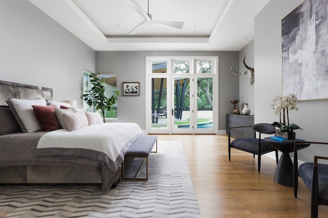 bedroom with access to outside, french doors, light wood-type flooring, a tray ceiling, and ceiling fan