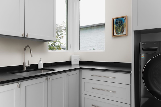 kitchen featuring washer / dryer, white cabinetry, and sink