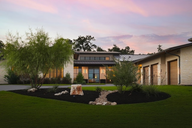 back house at dusk featuring a garage and a yard