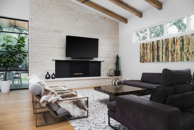 living room featuring light wood-type flooring, vaulted ceiling with beams, and a stone fireplace