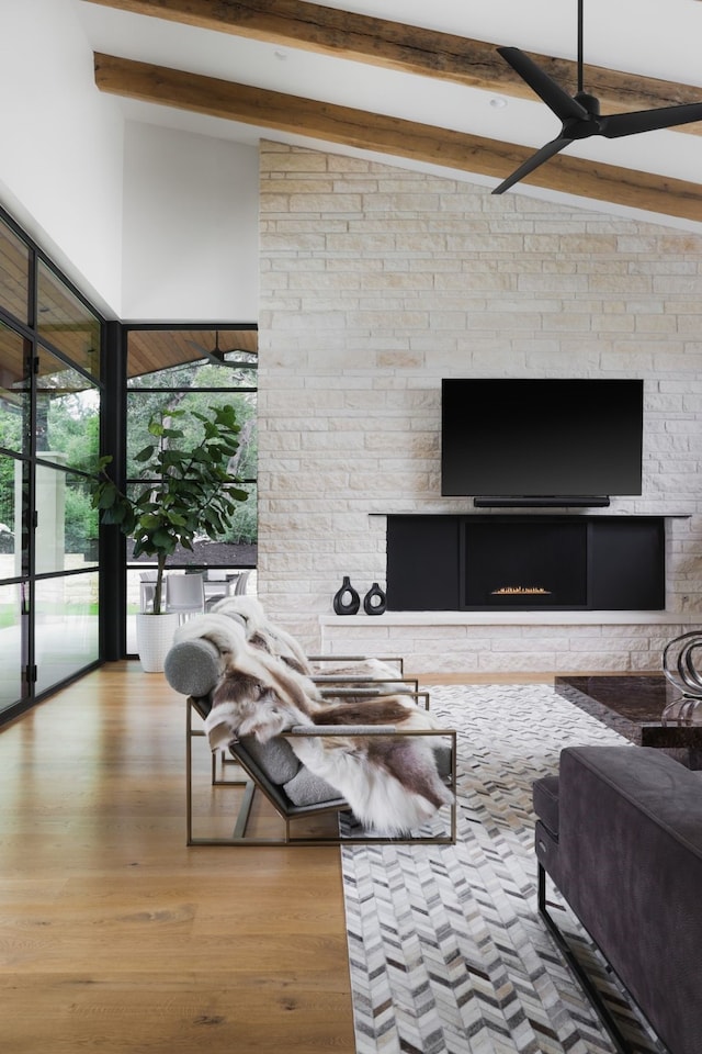 living room with ceiling fan, light wood-type flooring, vaulted ceiling with beams, and a stone fireplace