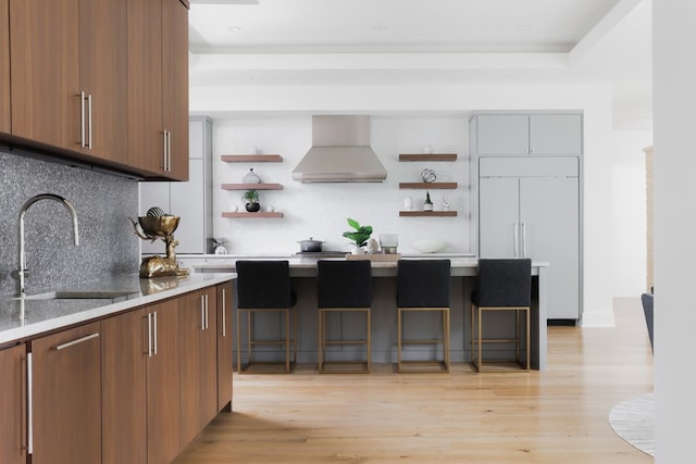 kitchen with sink, a kitchen bar, tasteful backsplash, paneled refrigerator, and wall chimney range hood