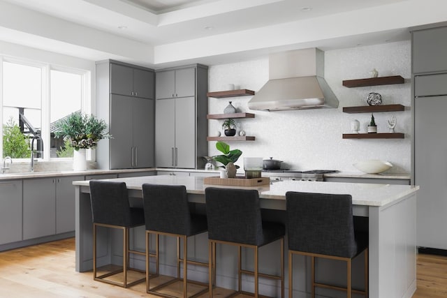 kitchen featuring a kitchen breakfast bar, light hardwood / wood-style flooring, custom exhaust hood, backsplash, and a kitchen island