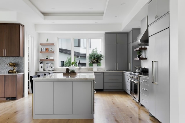 kitchen featuring a center island, a raised ceiling, wall chimney range hood, gray cabinets, and high end stove