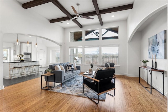 living room featuring ceiling fan, light hardwood / wood-style flooring, coffered ceiling, and beam ceiling