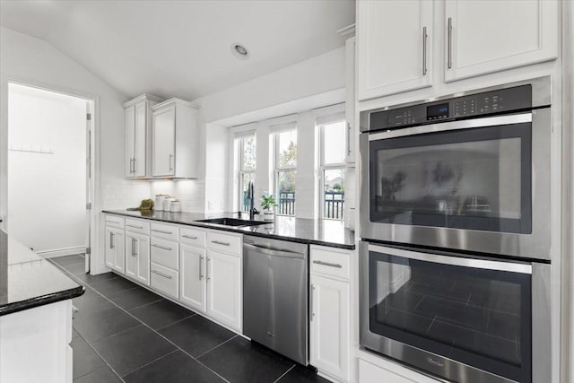 kitchen with stainless steel appliances, sink, white cabinetry, lofted ceiling, and decorative backsplash