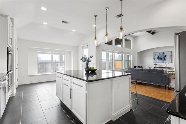 kitchen featuring hanging light fixtures, dark tile patterned floors, a kitchen island, lofted ceiling, and white cabinetry