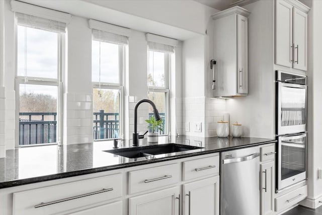 kitchen with decorative backsplash, white cabinetry, appliances with stainless steel finishes, dark stone countertops, and sink