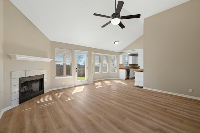 unfurnished living room with a tile fireplace, light wood-type flooring, high vaulted ceiling, and ceiling fan