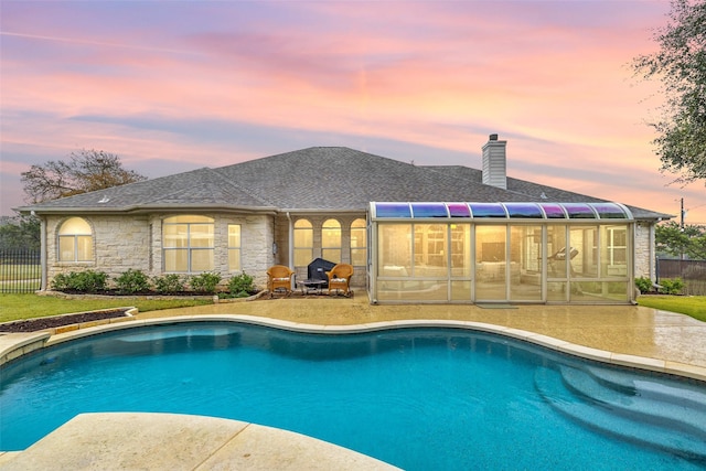 pool at dusk featuring a patio and a sunroom